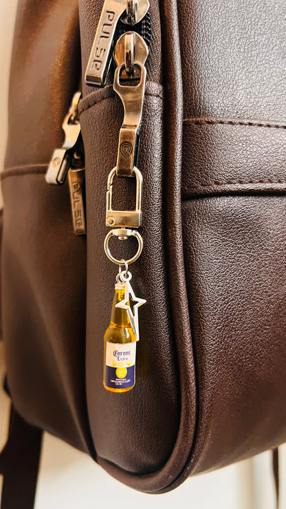 Mini Corona Extra bottle bag charm with silver star on a clasp, on a brown leather backpack
