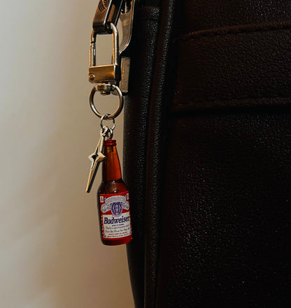 Mini Budweiser bottle charm with star pendant hanging on a black bag
