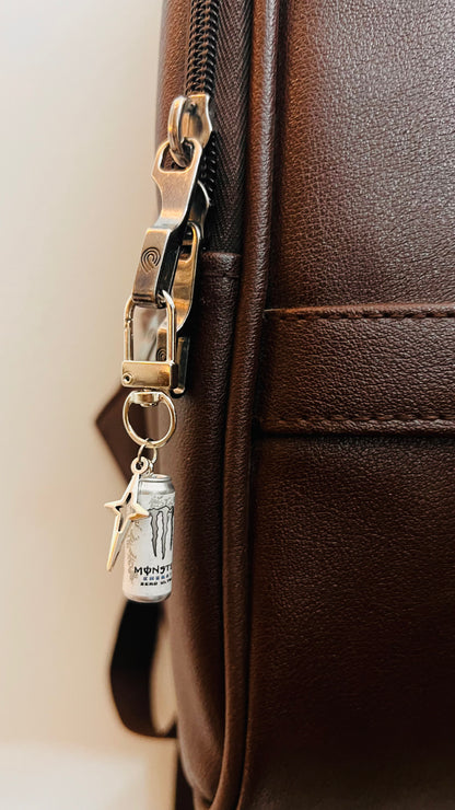 White Monster Energy can charm with silver star on a D-hook clasp, brown leather backpack