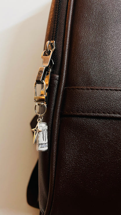 White Monster Energy can bag charm with star pendant on a D-hook, side view on a brown bag