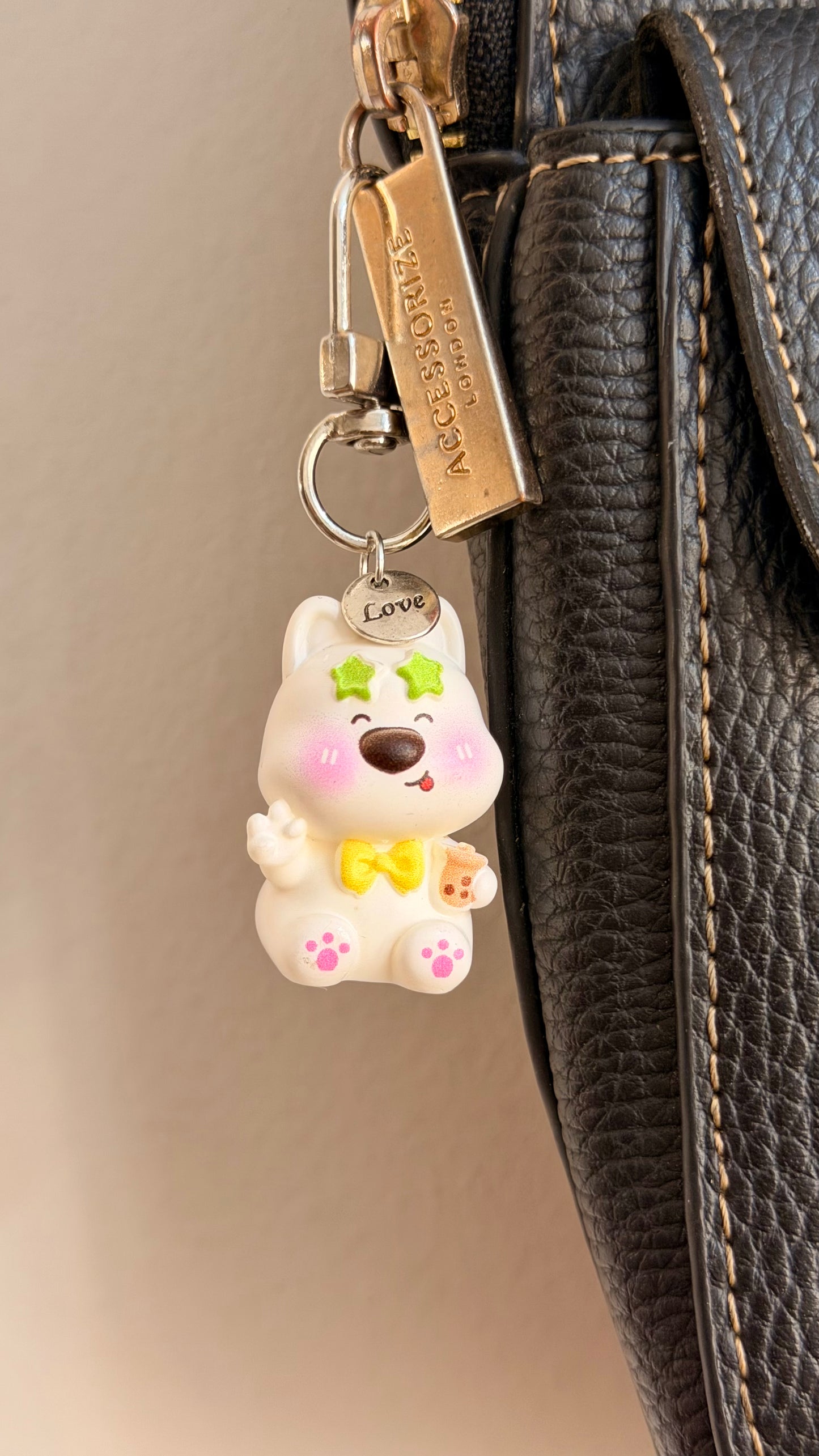 In my Boba Era, a white puppy in green star sunglasses holding a boba cup clipped to a black leather handbag zip.