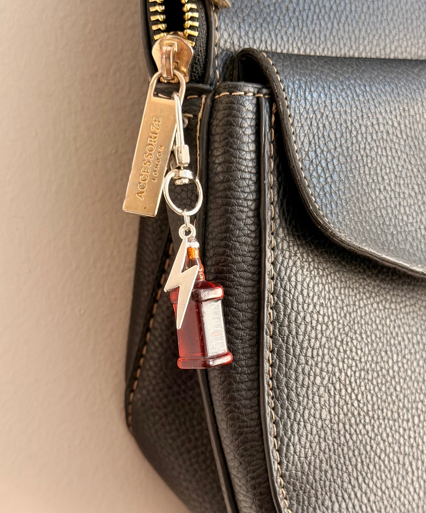 Jack daniels with Thunderbolt, a miniature whiskey bottle with a silver thunderbolt charm clipped to a black leather handbag zip.