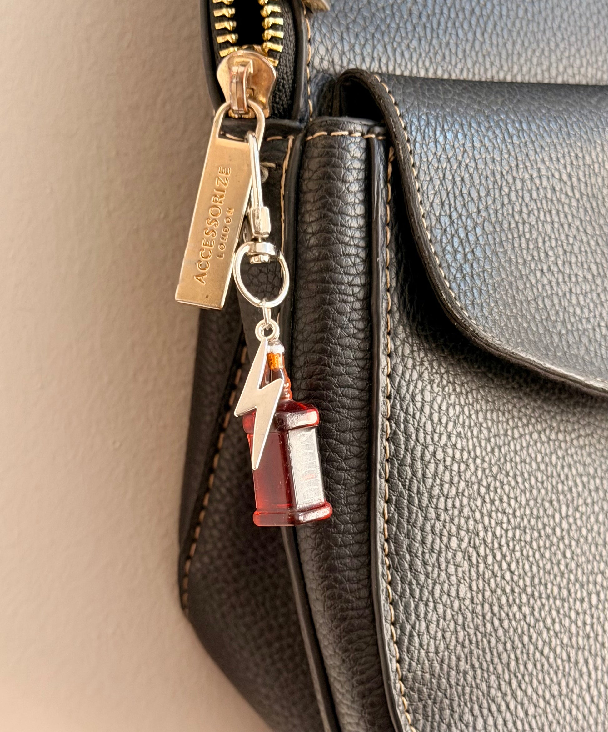 Jack daniels with Thunderbolt, a miniature whiskey bottle with a silver thunderbolt charm clipped to a black leather handbag zip.