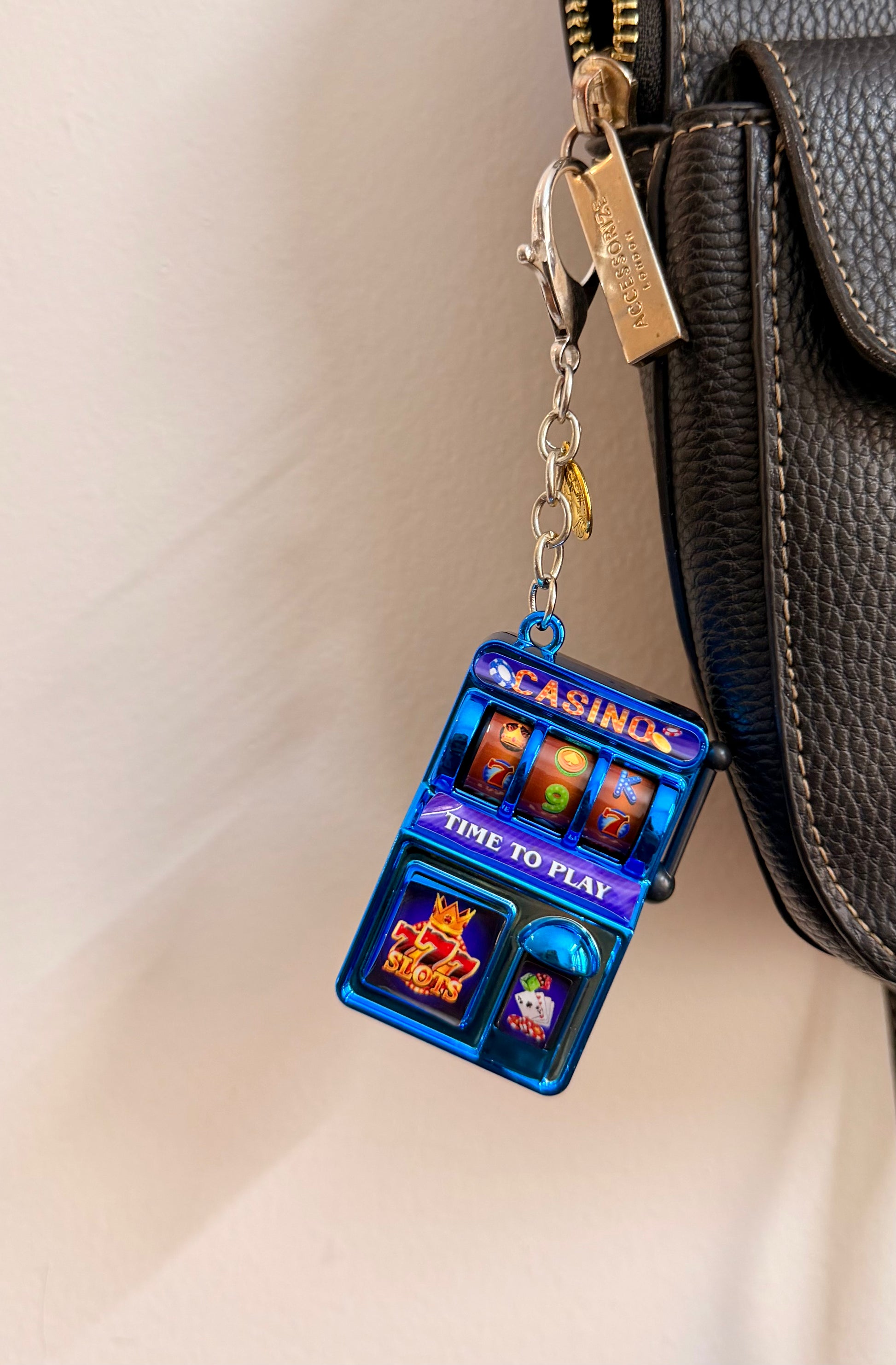 Jackpot, a blue casino slot machine charm with coin charms clipped to a black leather handbag zip.