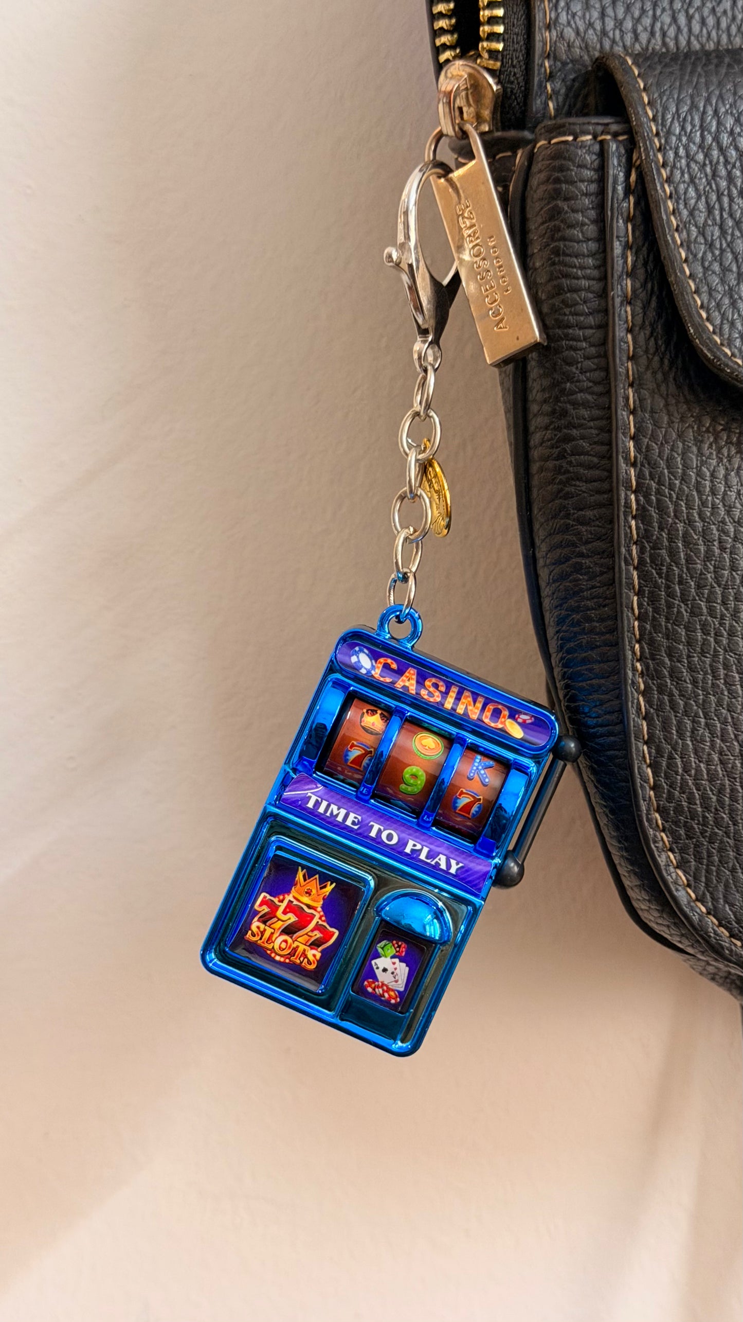 Jackpot, a blue casino slot machine charm with coin charms clipped to a black leather handbag zip.