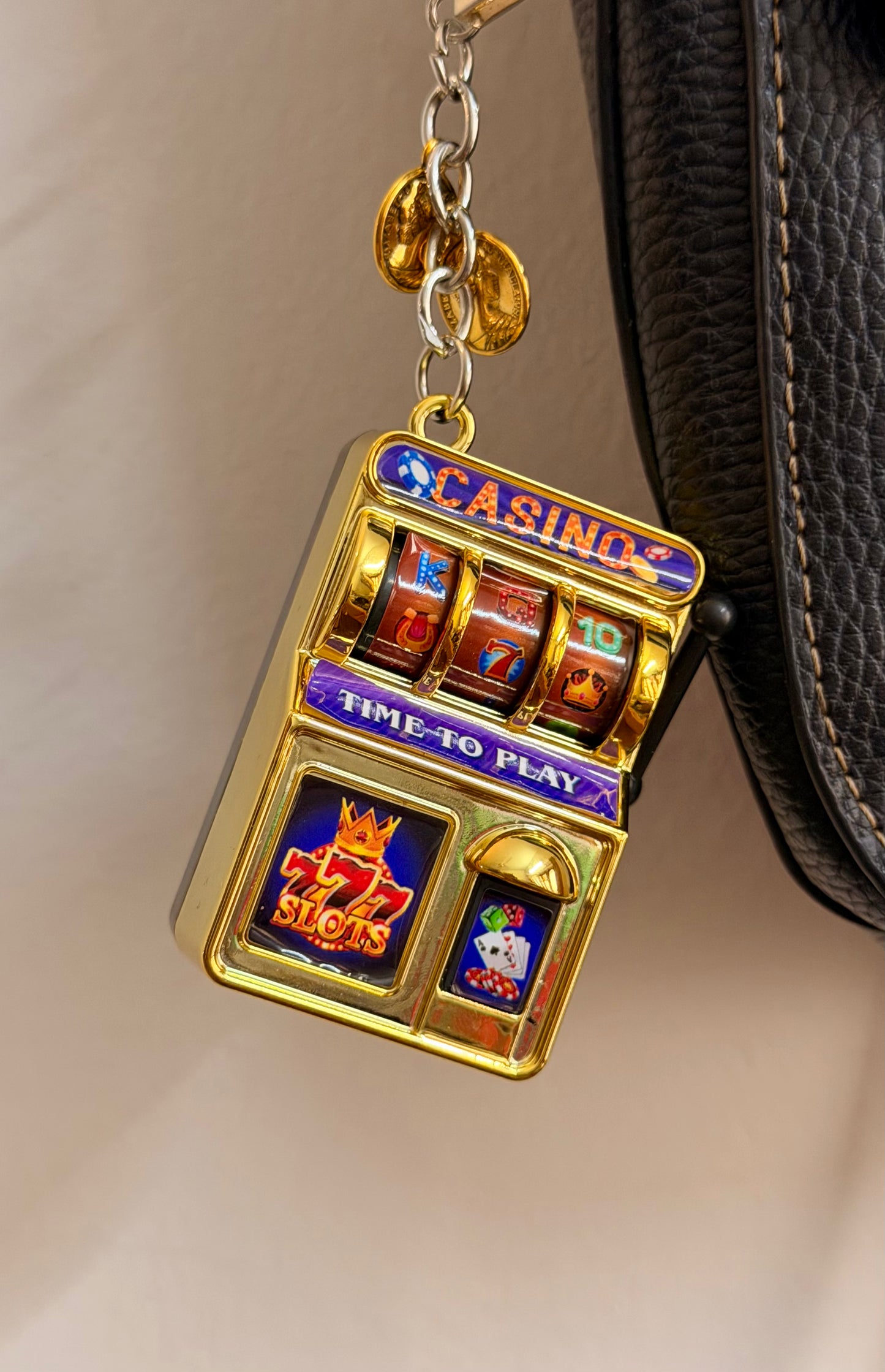 Jackpot, a gold casino slot machine charm with coin charms clipped to a black leather handbag zip.