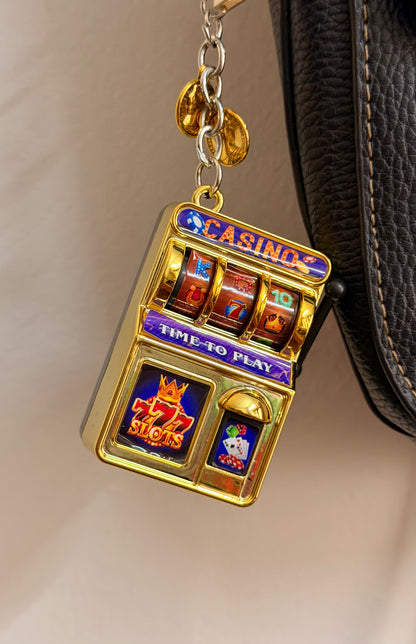 Jackpot, a gold casino slot machine charm with coin charms clipped to a black leather handbag zip.