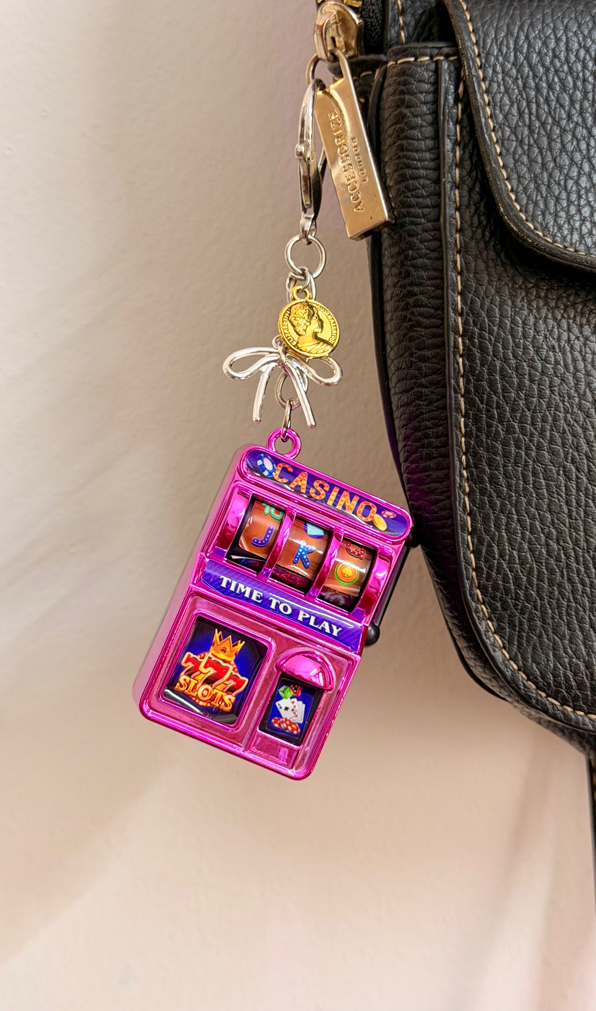 Jackpot, a pink casino slot machine charm with coin charms clipped to a black leather handbag zip.