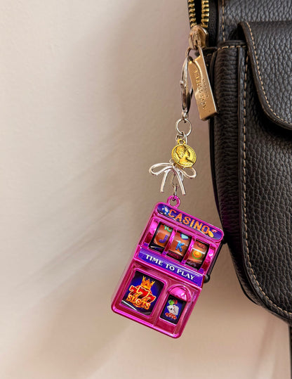 Jackpot, a pink casino slot machine charm with coin charms clipped to a black leather handbag zip.