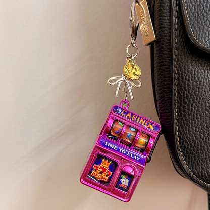 Jackpot, a pink casino slot machine charm with coin charms clipped to a black leather handbag zip.