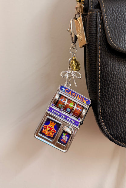 Jackpot, a silver casino slot machine charm with coin charms clipped to a black leather handbag zip.