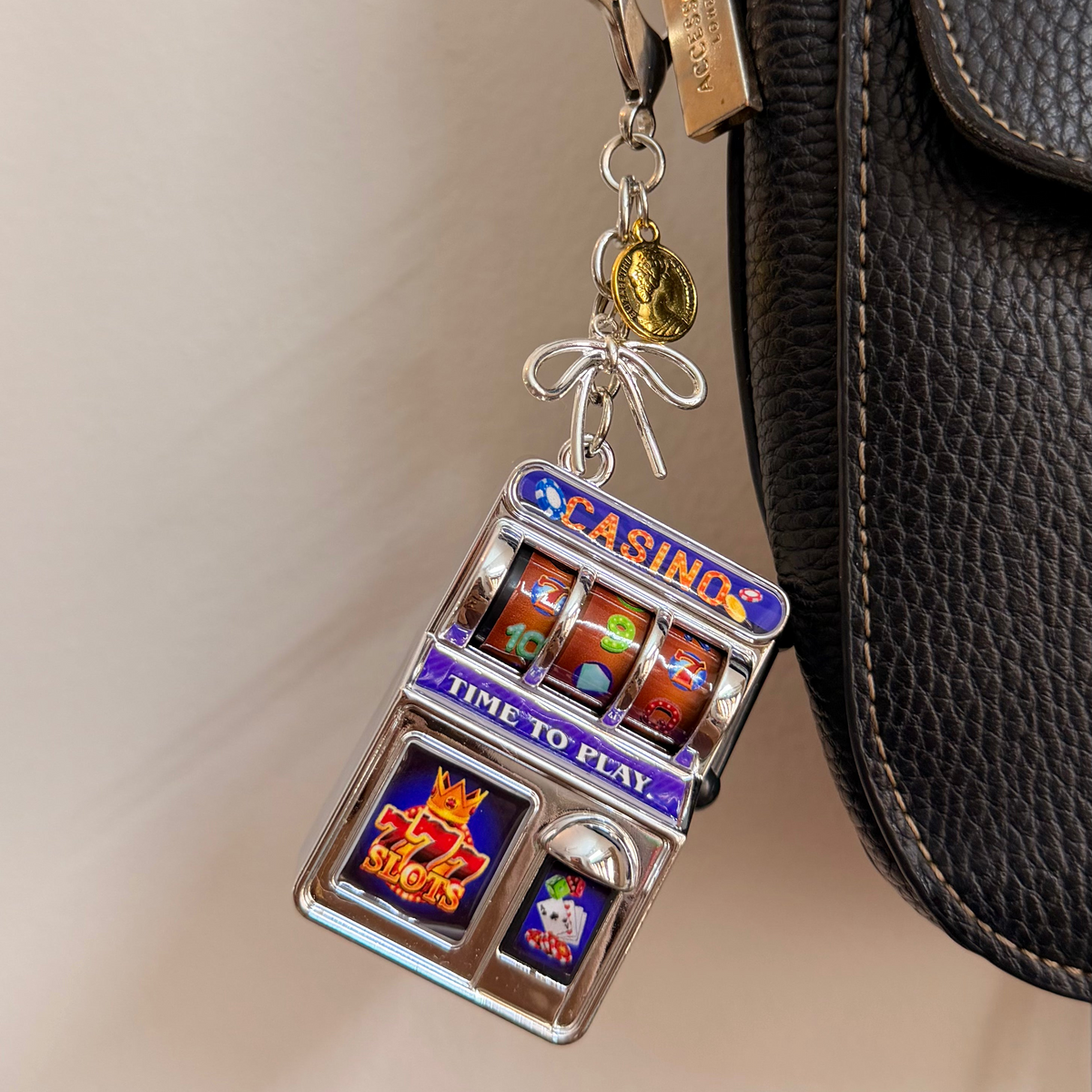 Jackpot, a silver casino slot machine charm with coin charms clipped to a black leather handbag zip.