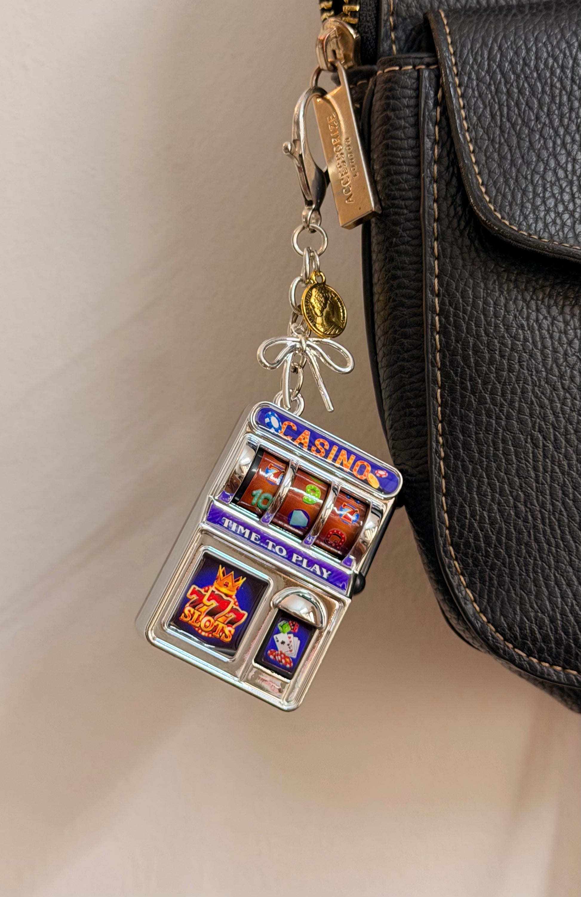 Jackpot, a silver casino slot machine charm with coin charms clipped to a black leather handbag zip.