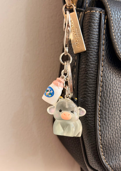 Moo-d Swing, a grey cow with a small bottle of milk clipped to a black leather handbag zip.