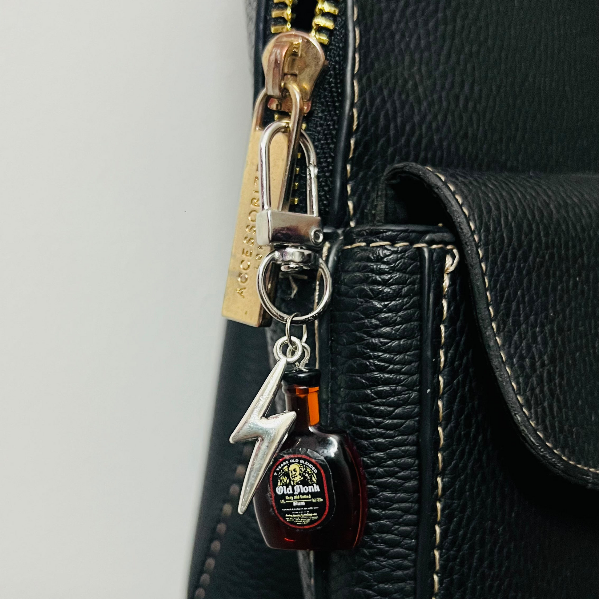 Old Monk rum bottle bag charm with a silver thunderbolt charm