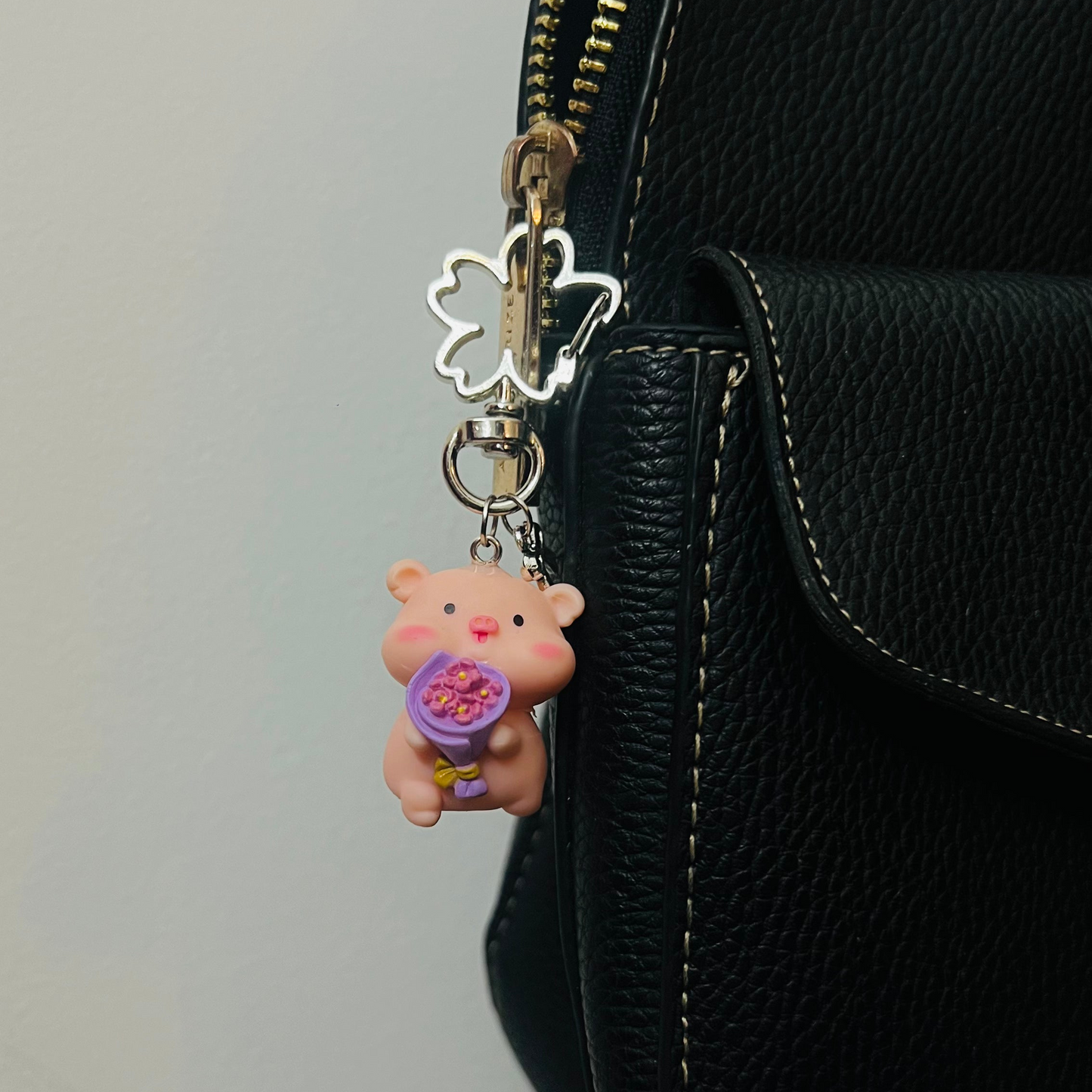 Pink Piggu piglet bag charm holding a purple bouquet of flowers