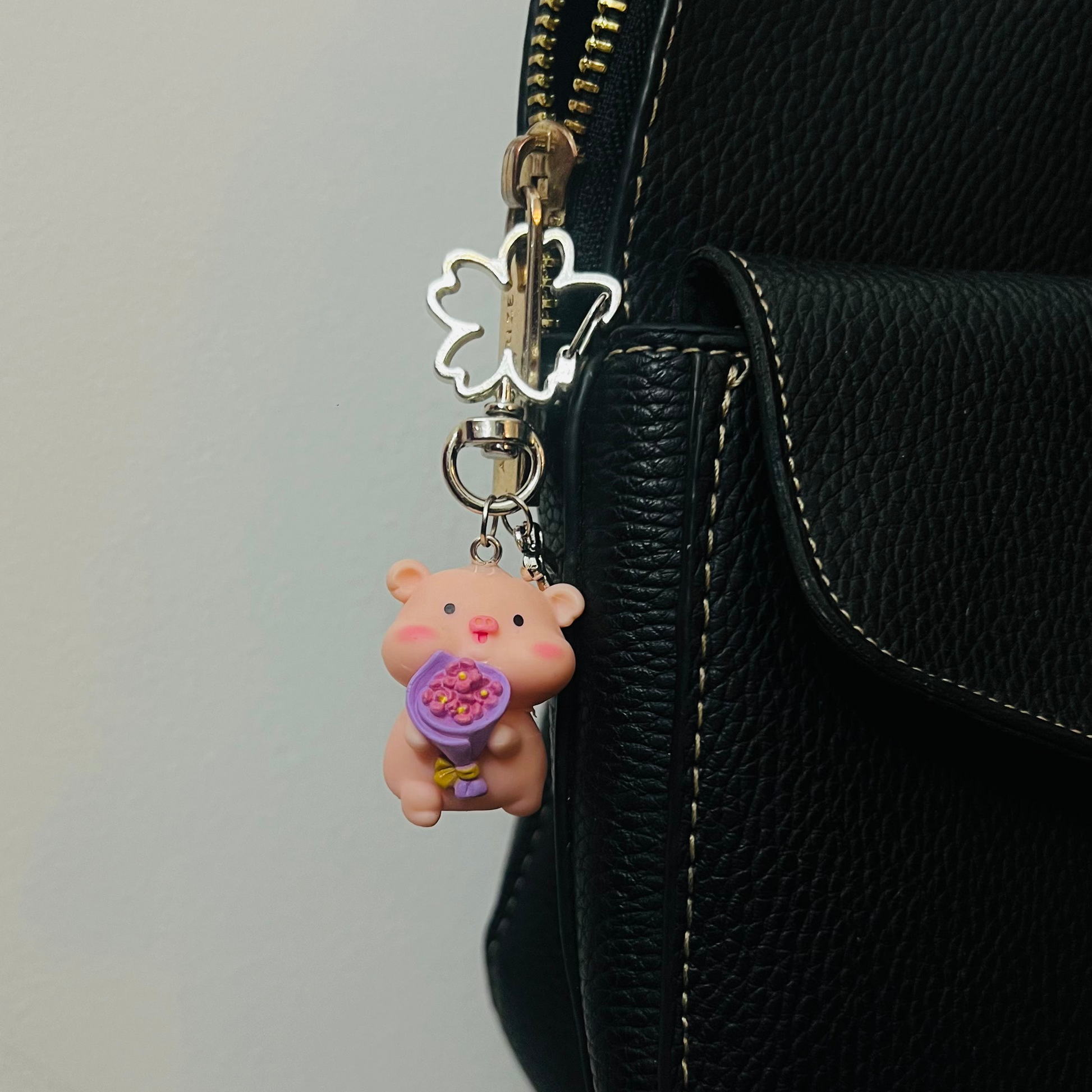 Pink Piggu piglet bag charm holding a purple bouquet of flowers
