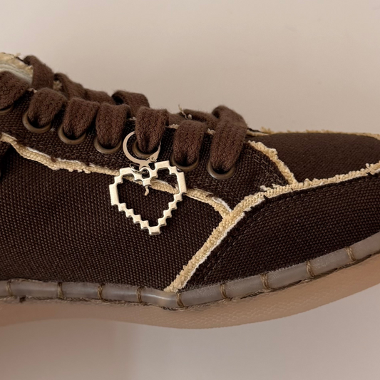 Pixel Heart Shoe Charm, open silver pixel heart charm on the laces of a brown canvas sneaker