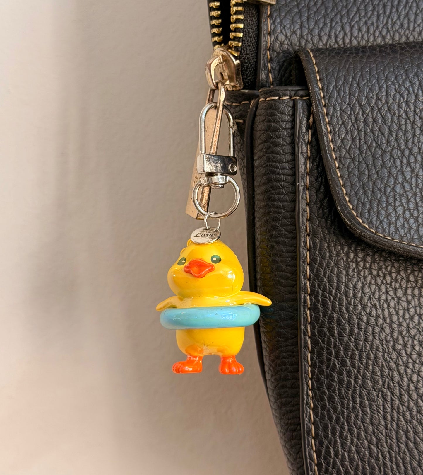 Pool Party Duck, a yellow duck in a pale blue swim ring clipped to a black leather handbag zip.