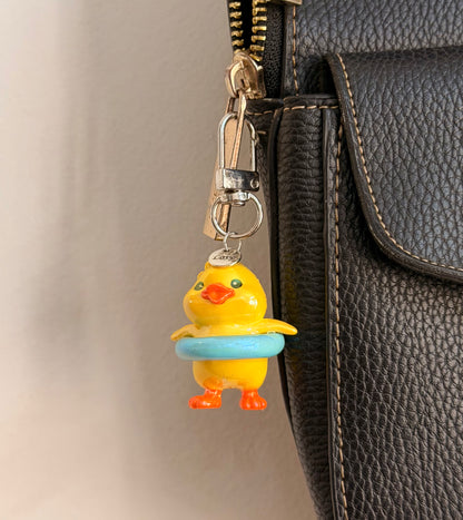 Pool Party Duck, a yellow duck in a pale blue swim ring clipped to a black leather handbag zip.