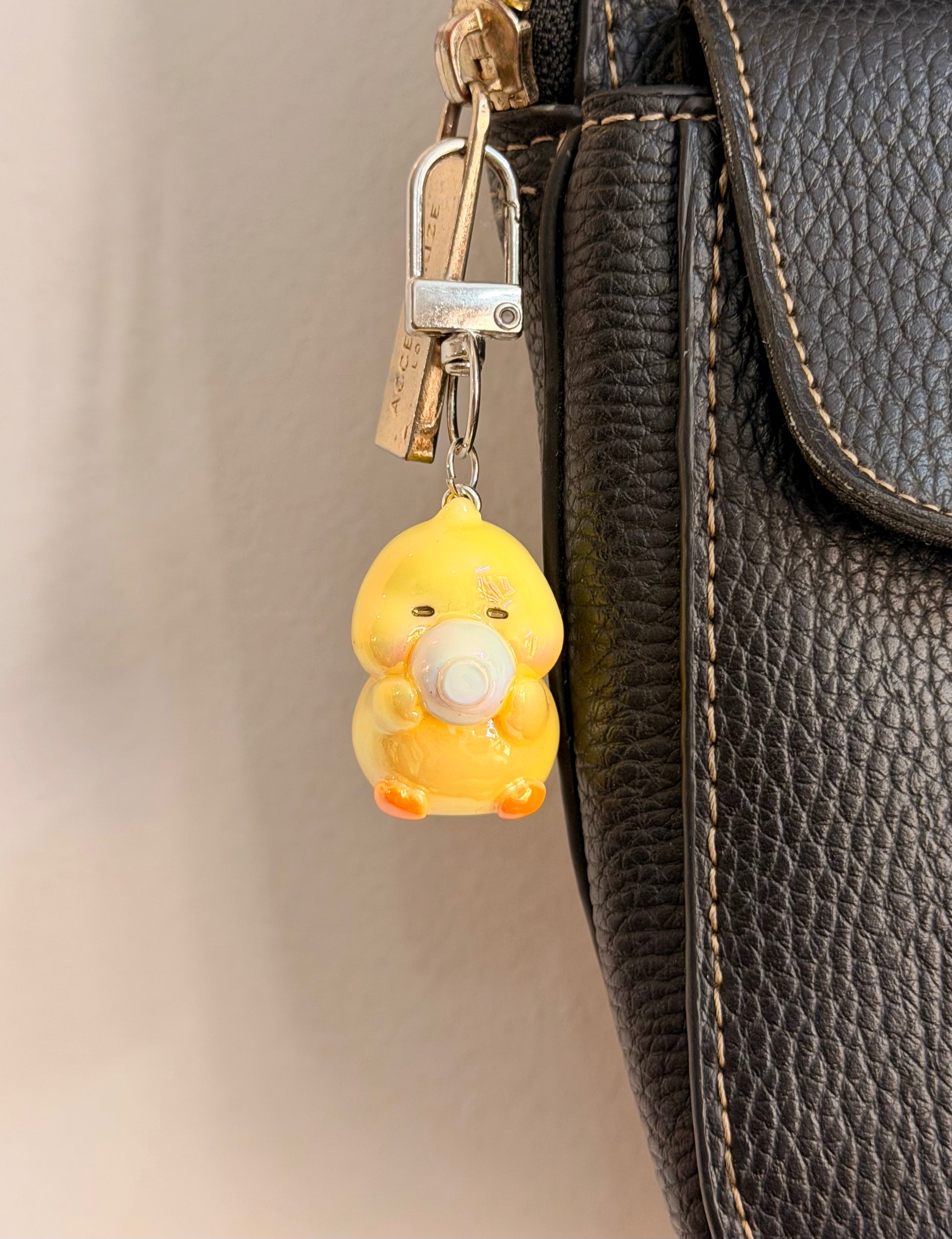 Quack & Snack, a yellow duck holding a white saucer clipped to a black leather handbag zip.