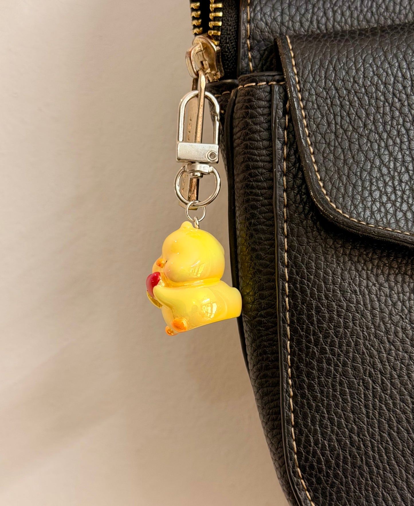 Quack in love, a yellow duck holding a red heart clipped to a black leather handbag zip.