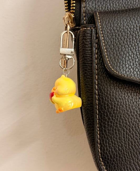 Quack in love, a yellow duck holding a red heart clipped to a black leather handbag zip.