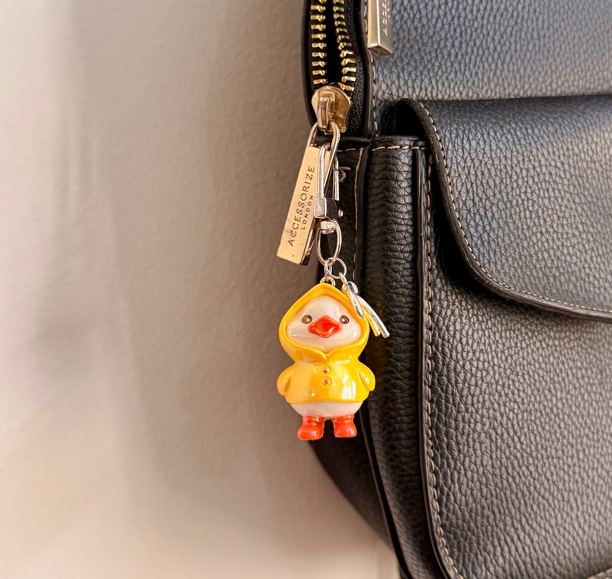 Rainy Day Duck, a yellow duck in a raincoat with the hood up and orange boots clipped to a black leather handbag zip.