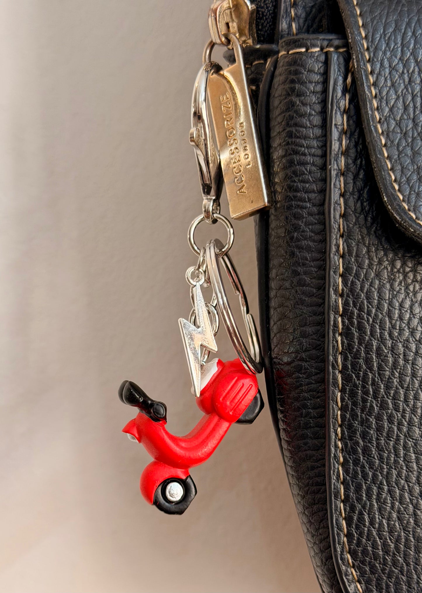 Red Vespa bag charm, a red scooter with a silver thunderbolt charm clipped to a black leather handbag zip.