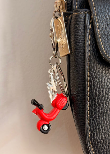 Red Vespa bag charm, a red scooter with a silver thunderbolt charm clipped to a black leather handbag zip.
