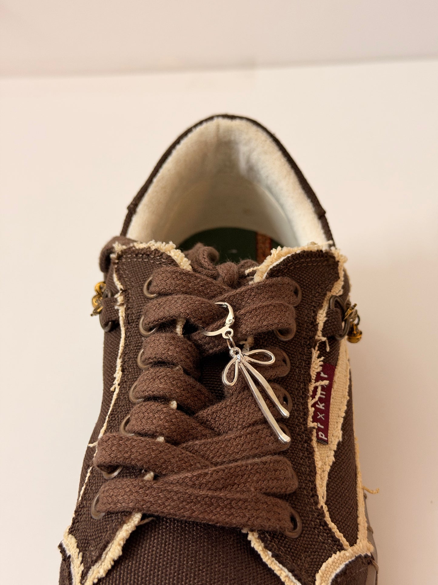 Boww Shoe Charm, fine-wire silver bow charm on the laces of a brown canvas sneaker
