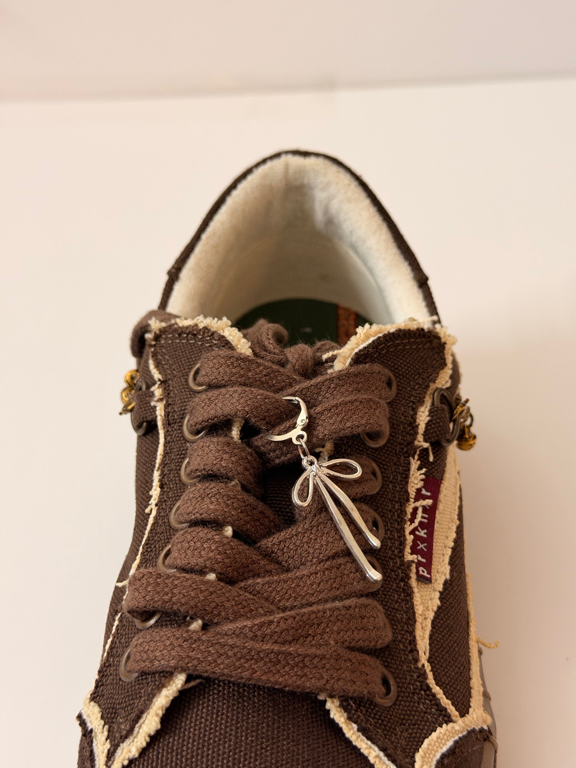 Boww Shoe Charm, fine-wire silver bow charm on the laces of a brown canvas sneaker