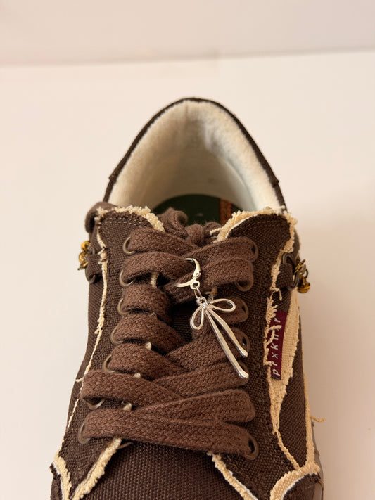 Boww Shoe Charm, fine-wire silver bow charm on the laces of a brown canvas sneaker