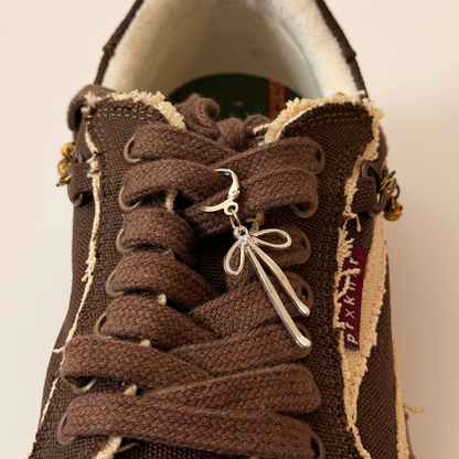Boww Shoe Charm, fine-wire silver bow charm on the laces of a brown canvas sneaker