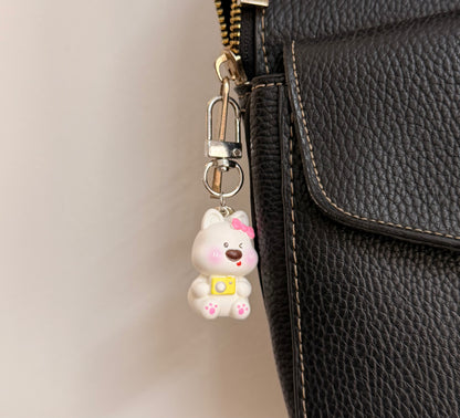 Say Cheese, a white puppy with a pink bow and a yellow camera clipped to a black leather handbag zip.