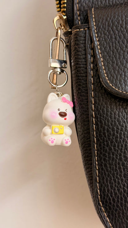 Say Cheese, a white puppy with a pink bow and a yellow camera shown from another angle.