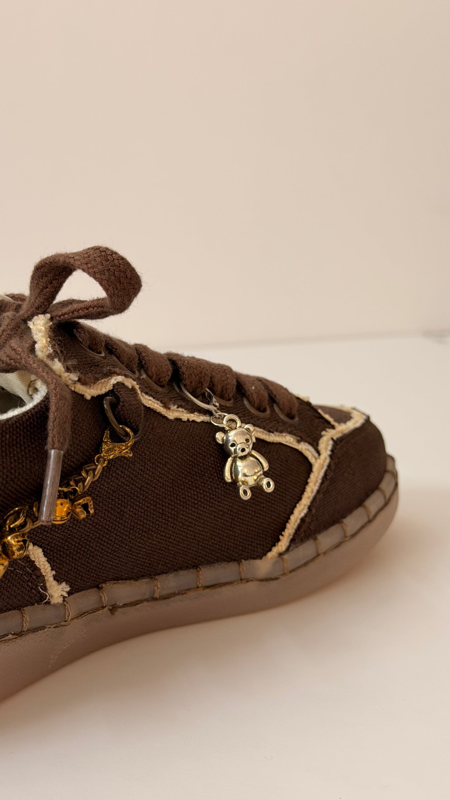 Silver Teddy Shoe Charm, polished silver teddy bear charm on the laces of a brown canvas sneaker