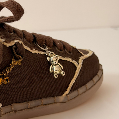 Silver Teddy Shoe Charm, polished silver teddy bear charm on the laces of a brown canvas sneaker
