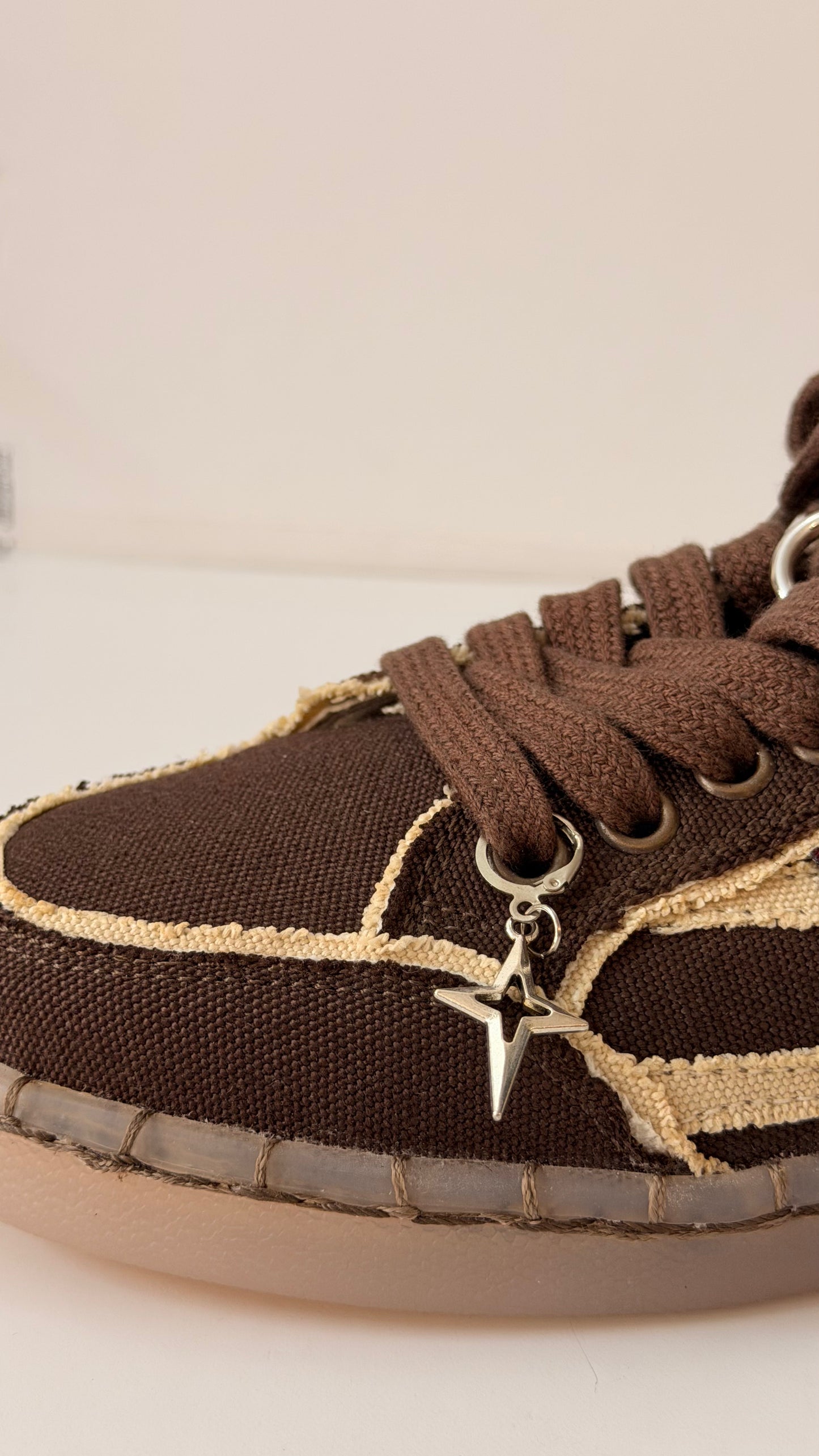 Star Bling Shoe Charm, silver four-point star charm with a cut-out centre on the laces of a brown canvas sneaker, side view