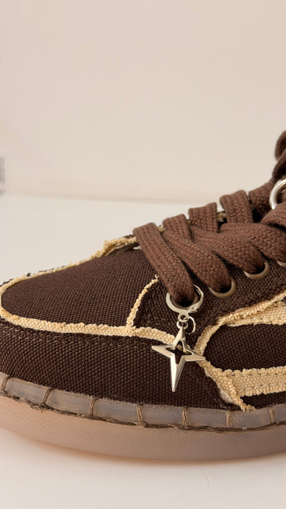 Star Bling Shoe Charm, silver four-point star charm with a cut-out centre on the laces of a brown canvas sneaker, side view