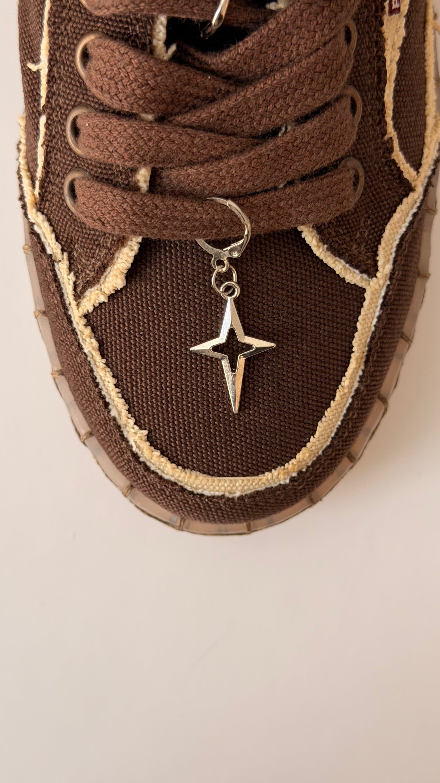 Star Bling Shoe Charm, silver four-point star charm with a cut-out centre on the laces of a brown canvas sneaker
