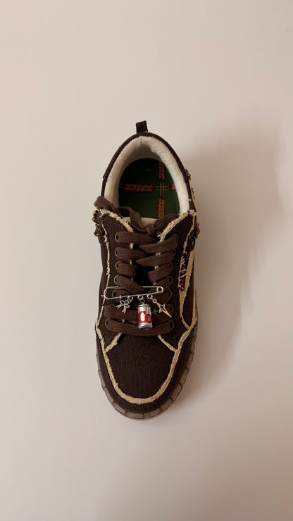 The Pop Charm, brooch pin fastened to the laces of a brown canvas sneaker
