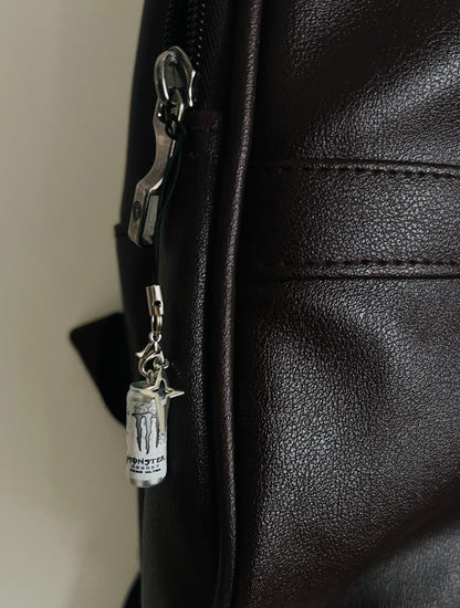 White Monster Energy can charm with silver star on a clasp, clipped to a dark brown backpack