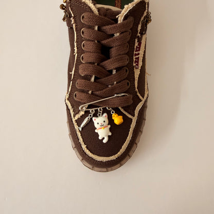 White Cat Charm, brooch pin fastened to the laces of a brown canvas sneaker