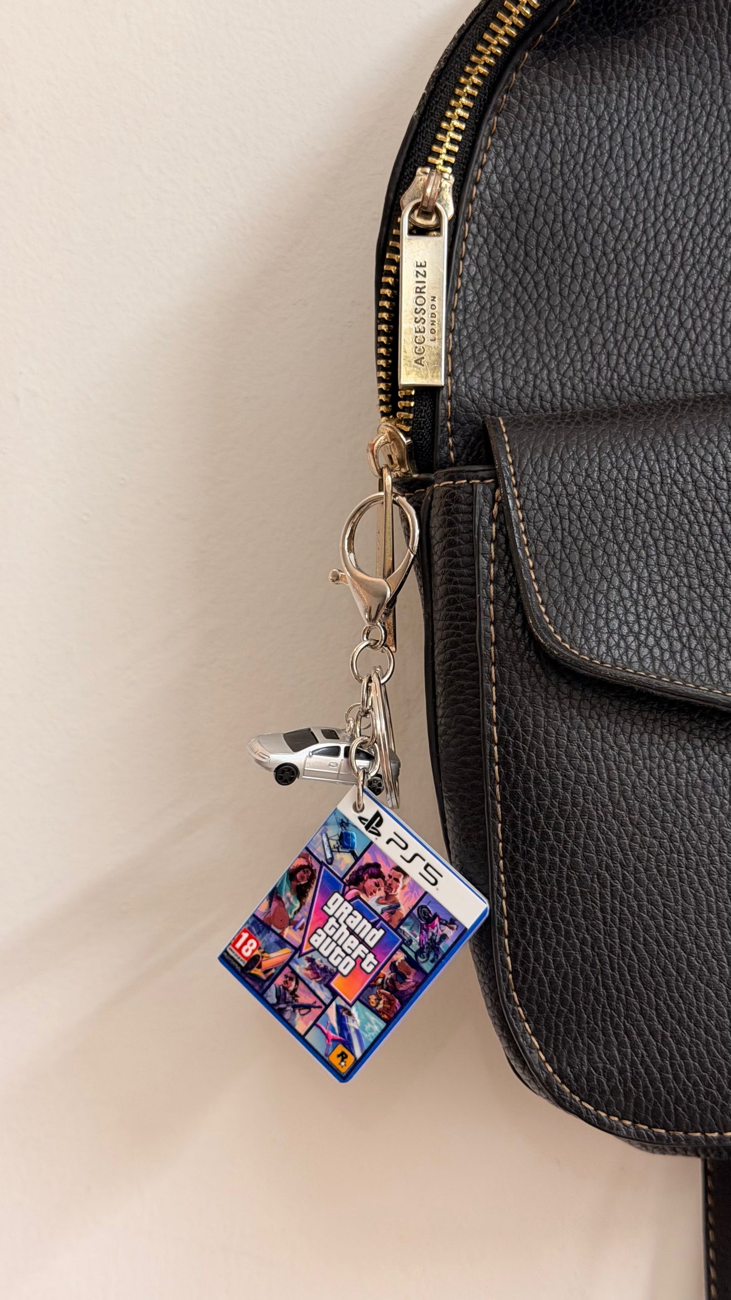 Here We Go Again, GTA 6 game case charm with a silver car clipped to a black leather bag