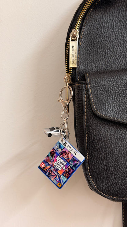 Here We Go Again, GTA 6 game case charm with a silver car clipped to a black leather bag