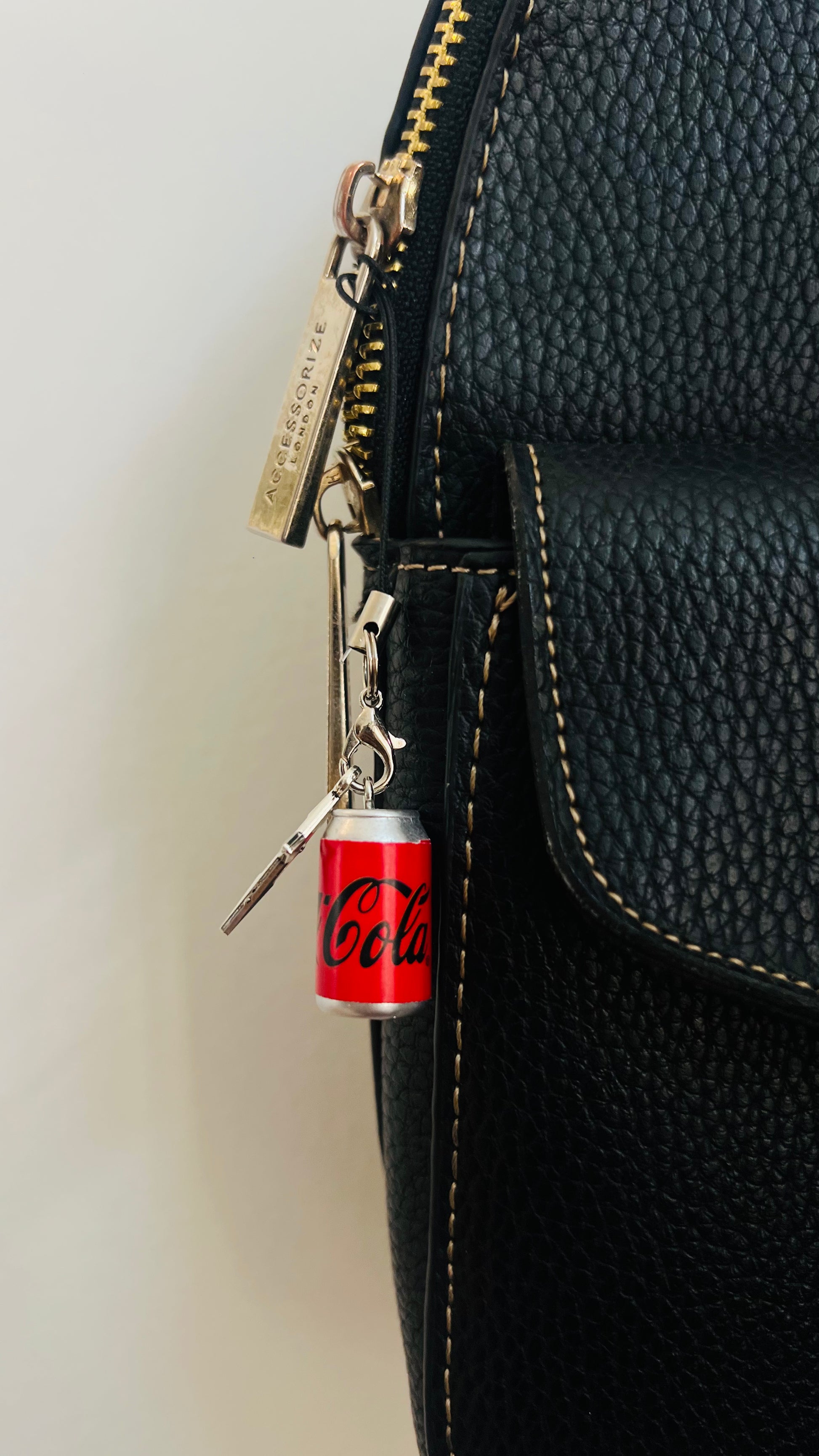Red Coca-Cola can charm with a silver star on a phone strap, clipped to a black bag